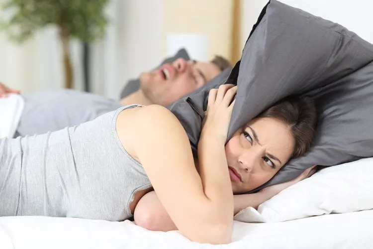 man snoring while his wife is covering ears with the pillow