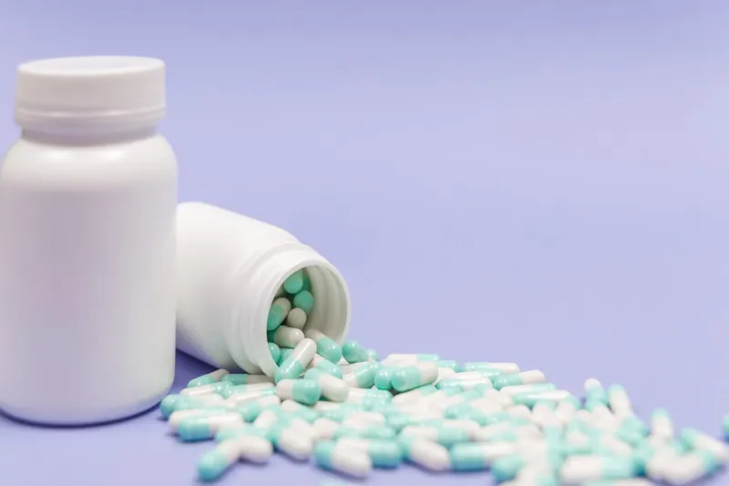 blue and white capsules pill spilled out from white plastic bottle container global healthcare concept antibiotics drug resistance antimicrobial capsule pills pharmaceutical industry pharmacy