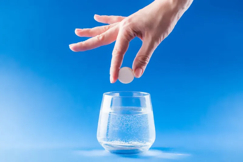 headache medicine woman hand puts aspirin into glass with water health care concept with blue background