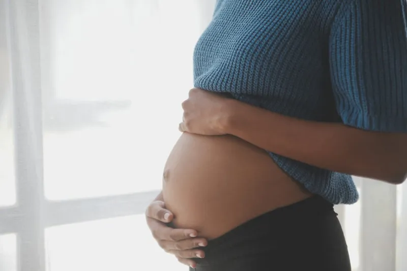 happy pregnant woman touching belly in front of white wall