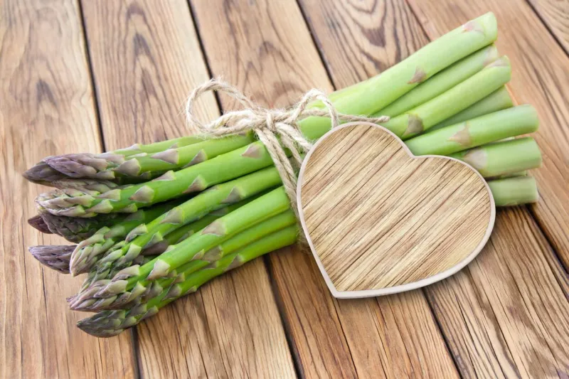 green asparagus and heart on wooden background