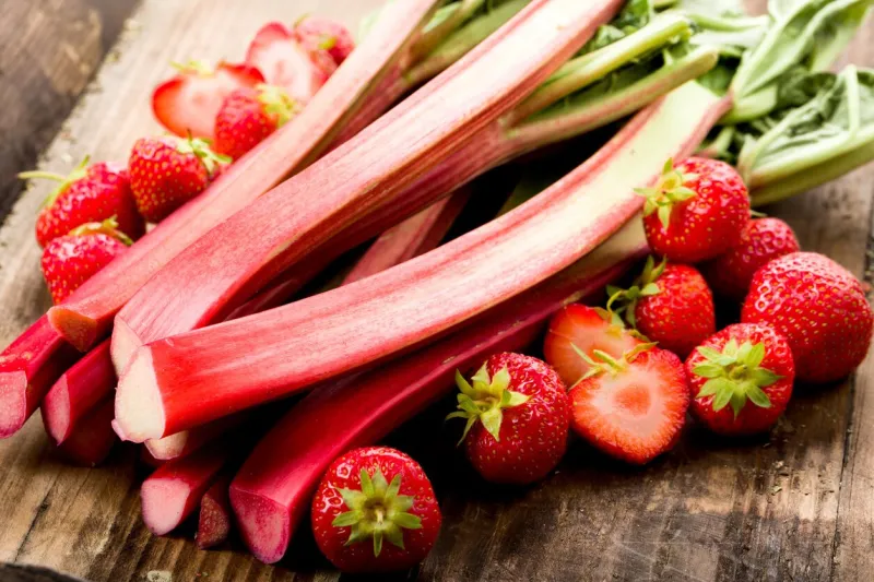 fresh rhubarb and strawberries on a wooden underground