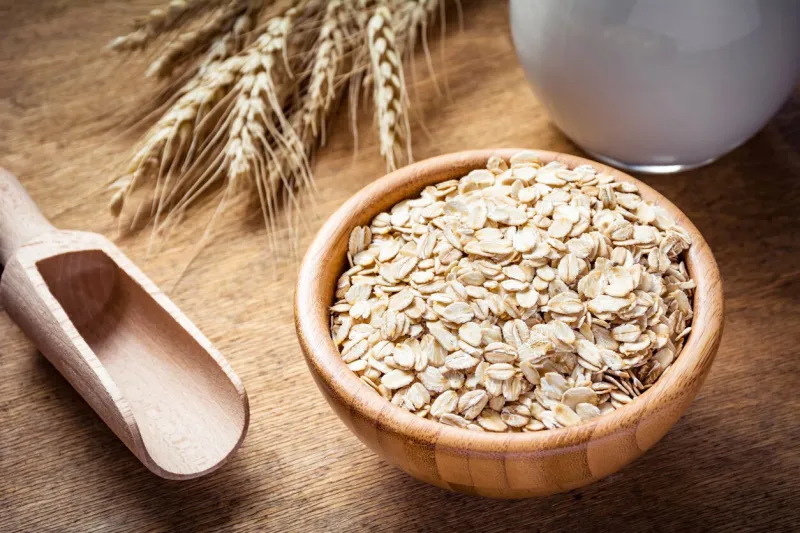 rolled oats (oat flakes), milk and golden wheat ears on wooden background raw food ingredients, healthy lifestyle, cooking food