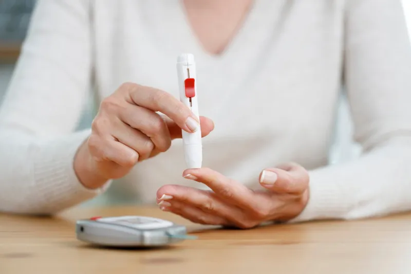 woman hands using lancet on finger to check blood sugar level by glucose meter medicine, diabetes, glycemia and health care concept