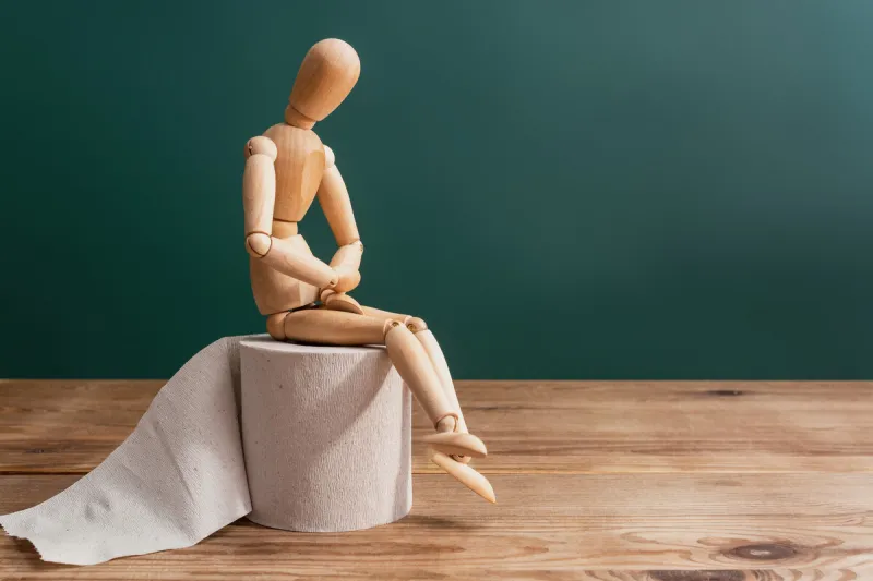 wooden figure sit on a roll of toilet paper concept of the problem with digestion