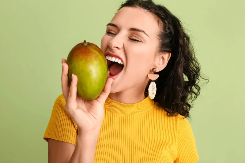 beautiful woman with fresh mango on color background