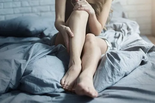female legs in bed, closeup woman body and skin care, tired legs after working day or fitness workout
