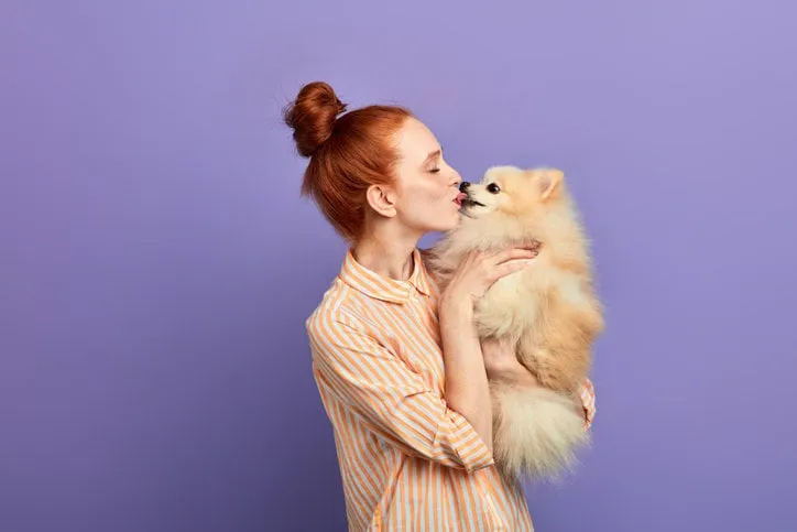 romantic moment, ginger girl kissing her dog close up side view photo closeness concept , isolated blue background