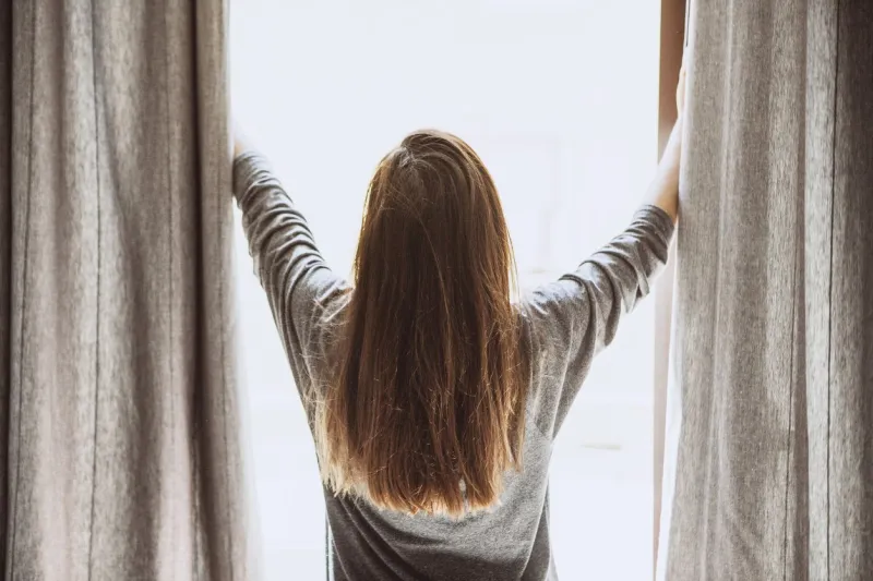 the girl opens the curtains in the morning