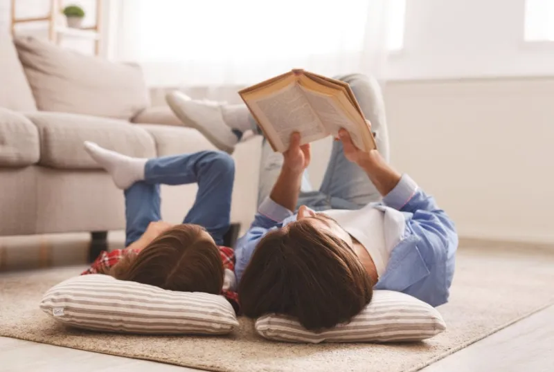 little daughter and daddy enjoying time together, laying on floor at home, man reading book to his cute daughter, empty space