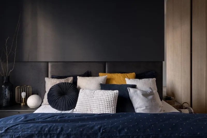 stylish bed with comfortable headboard and many pillows in modern dark bedroom