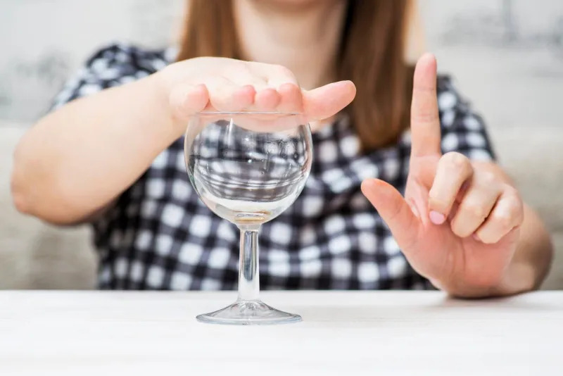 a woman's hand is shown gesturing 'no' to a glass of water, symbolizing alcohol refusal or a commitment to sobriety