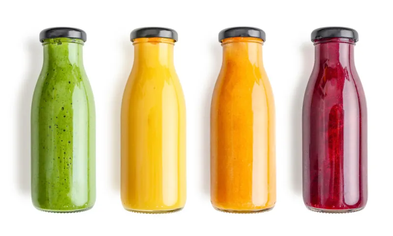 green, yellow, orange and red smoothie in glass bottles isolated on white background, top view clipping path included