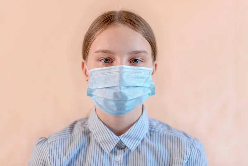 close-up portrait of a beautiful teenager 12-15 years old, covers his face wearing a medical blue mask, anti-coronavirus covid-19 pandemic infectious disease outbreak protection, healthcare concept