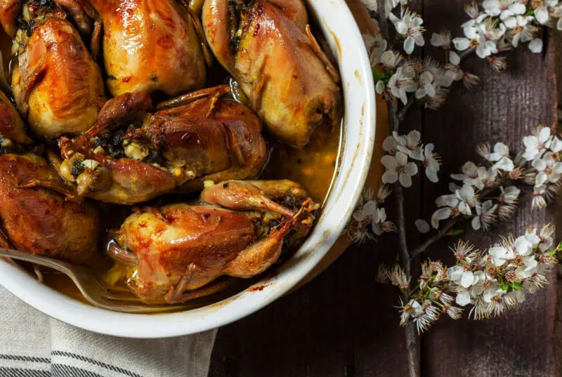 baked quail stuffed with mushrooms, eggs and bread in a ceramic form on a wooden table rustic style, selective focus