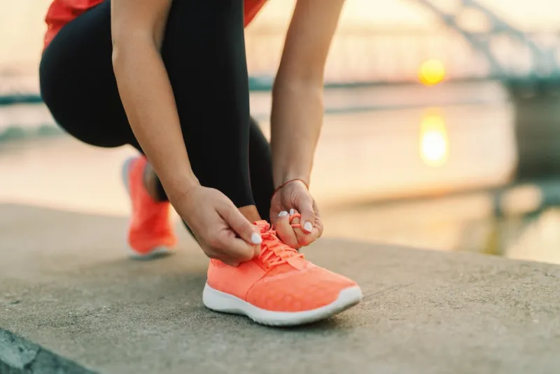 close up of sporty woman tying shoelace while kneeling outdoor, in background bridge fitness outdoors concept