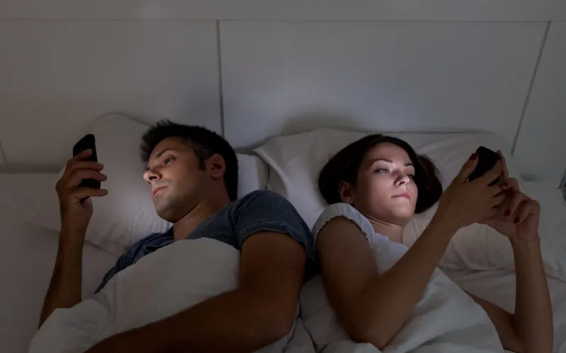 young couple with smartphones in their bed
