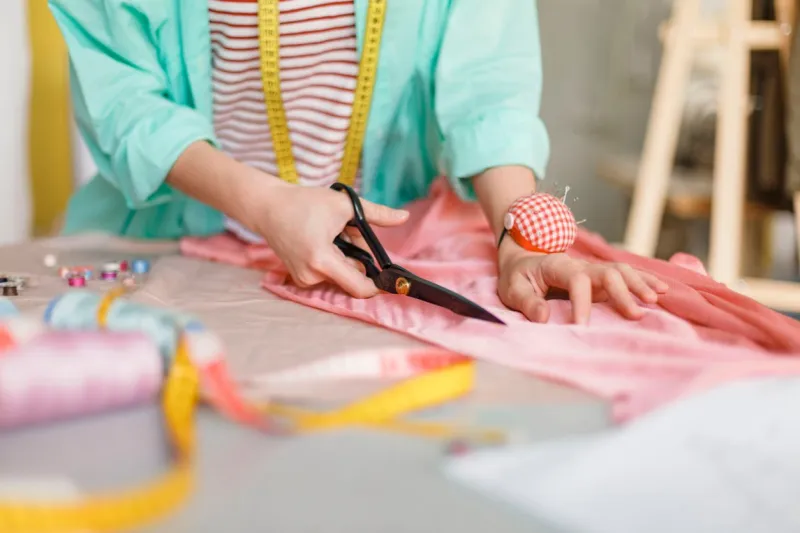 close up seamstress cutting fabric with scissors in modern sewing workshop