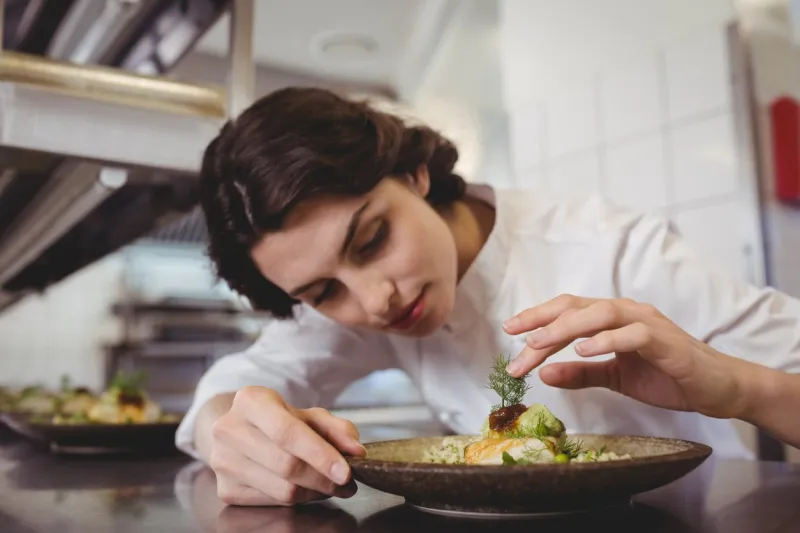 female chef examining appetizer plate at order station in restaurant