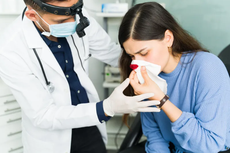 professional otolaryngologist trying to stop a nasal hemorrhage of a female patient latin woman suffering from a nosebleed at the doctor