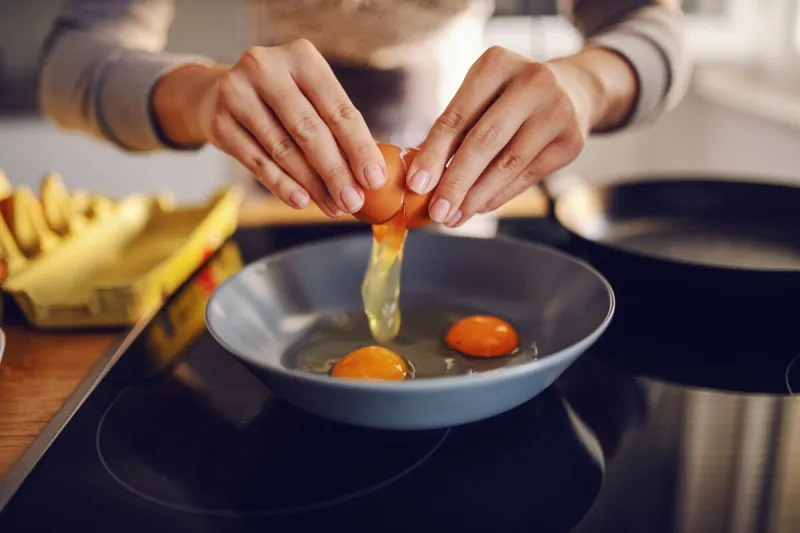 close up of caucasian woman breaking egg and making sunny side up eggs domestic kitchen interior breakfast preparation