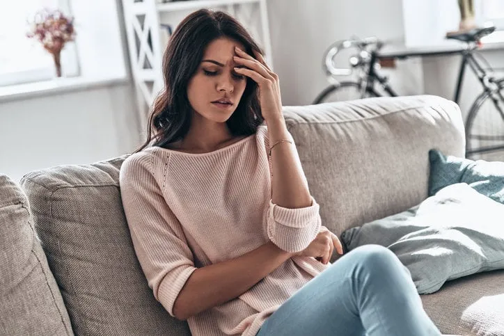 frustrated young woman suffering from the headache while sitting on the sofa at home