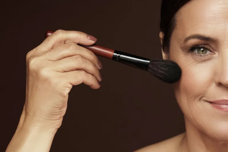 beautiful middle aged woman applying foundation powder or blush on her face