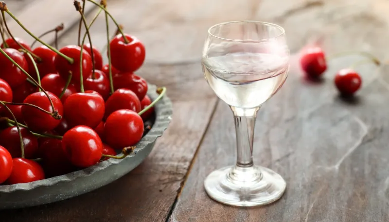 kirsch or kirschwasser - a strong alcoholic cherry drink in a glass and fresh cherry on an old dark wooden table