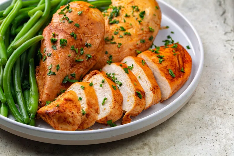 close-up of oven baked boneless chicken breast made with paprika and parsley, green beans