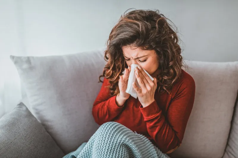 portrait of woman with allergy blowing her nose illness and sickness runny nose ill young blond woman having fever and blowing her nose while having a blanket portrait of a young woman sneezing in to tissue
