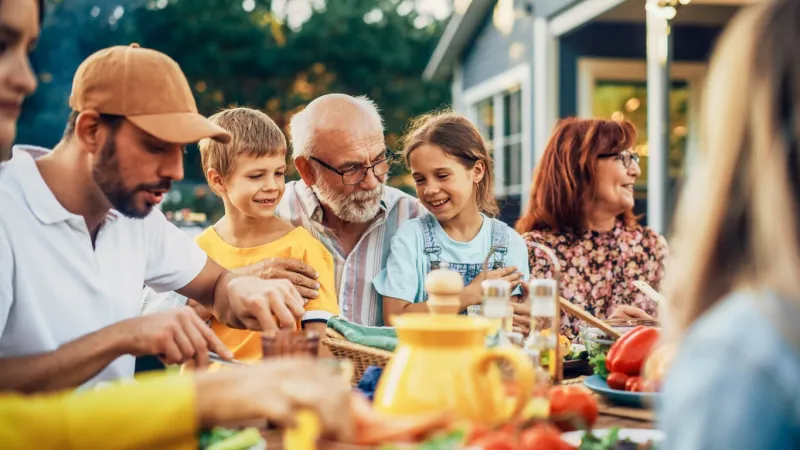 portrait of a happy senior grandfather holding his bright talented little grandchildren on lap at a outdoors dinner party with food and drinks family having a picnic together with children