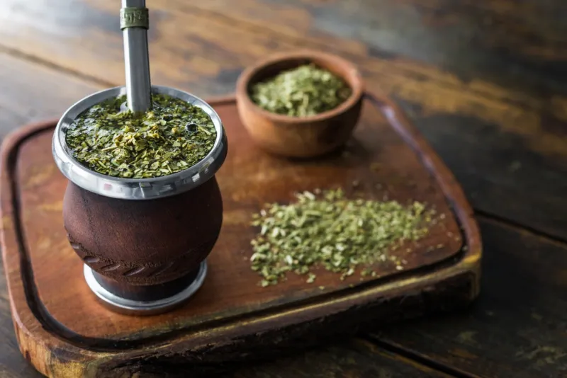 traditional argentinian yerba mate tea in a calabash gourd with bombilla stick against wooden background