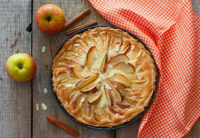 homemade apple cake with almond and cinnamon over natural wood background, top view