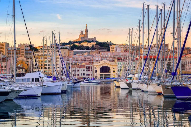 yachts reflecting in the still water of the old vieux port of marseilles beneath cathedral of notre dame, france, on sunrise