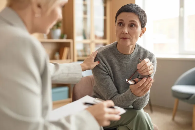 portrait of distressed mature woman listening to female psychologist during private therapy session