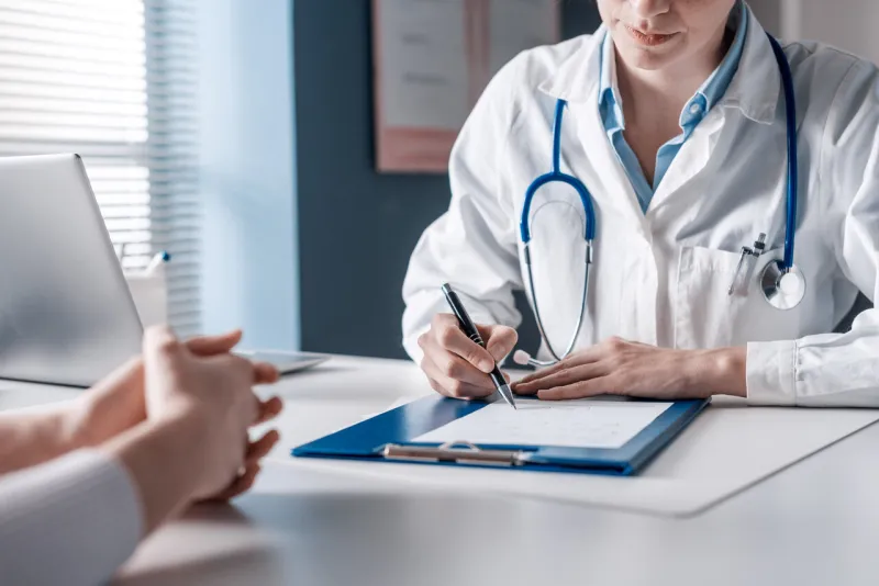doctor sitting at desk and writing a prescription for her patient