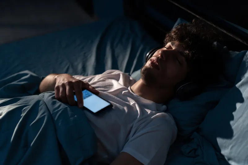 young arabic man listening to music while resting in bed at home at night copy space