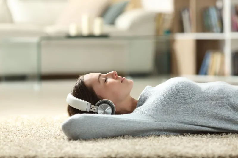 side view portrait of a relaxed woman listening to music with headphones lying on a carpet at home