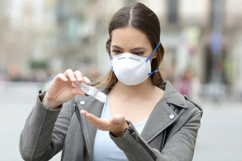 portrait of a serious girl wearing protective mask applying sanitizer hand rub preventing contagion on city street