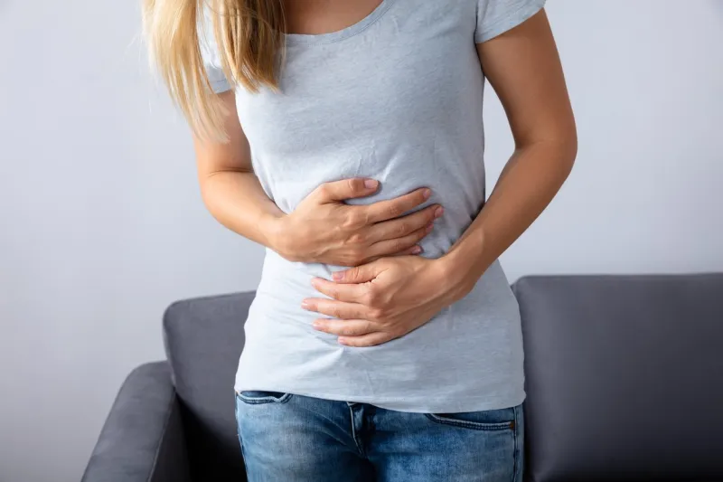 woman sitting on sofa suffering from stomach pain