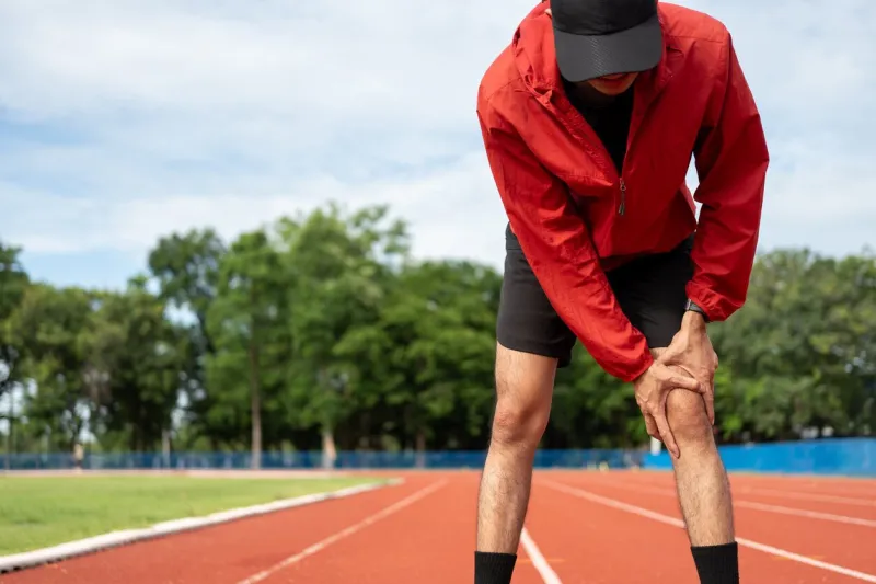 young man tired during jogging on the track in sport stadium runner has sore knees because he has been running for too long exercising until the injury training athlete work out at outdoor