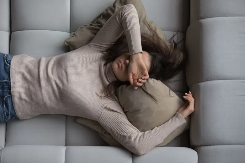 peaceful pretty 20s girl lying on back on comfortable couch at home, covering eyes with hand, sleeping at daytime, feeling tired, enjoying relaxation, leisure, break, weekend top view