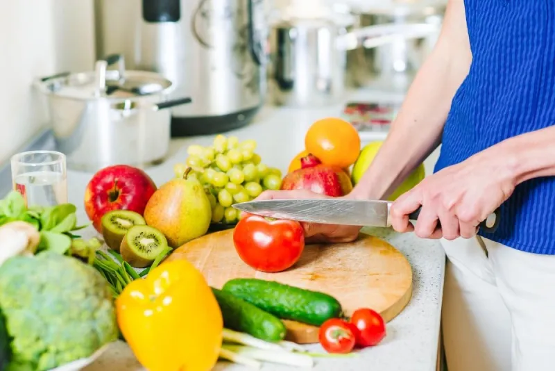 woman cuts tomatoe by the knife on the wooden board at the kitchen