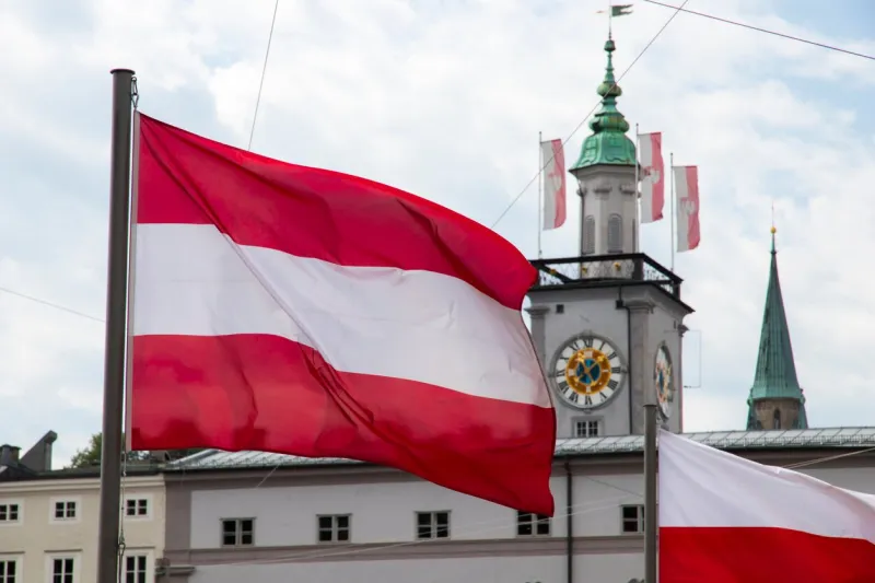 a waving flag of austria, with a flag of poland and salzburg town hall (rathaus) in the background