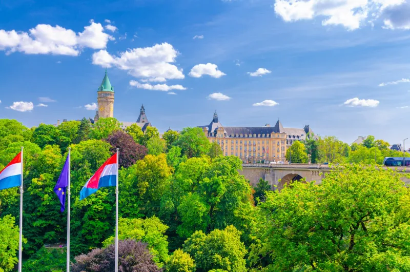 luxembourg city historical centre with luxembourg and eu flags on poles, pont adolphe bridge, petrusse parks green trees and state bank and savings bank spuerkeess on fort bourbon square