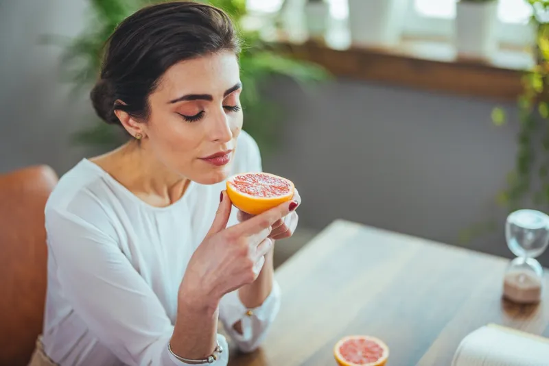 sick woman trying to sense smell of half fresh orange, has symptoms of covid-19, corona virus infection - loss of smell and taste one of the main signs of the disease
