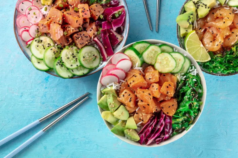 poke bowl variety, a close-up with chopsticks on a blue background healthy hawaiian dish with salmon, tuna, and shrimps, overhead flat lay shot