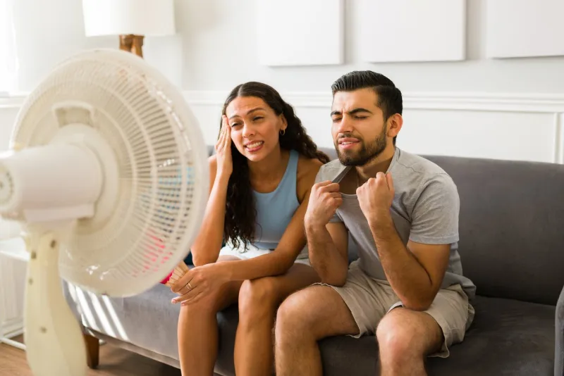 upset woman and man sweating and feeling very hot during the hot weather young couple turning on the electric fan