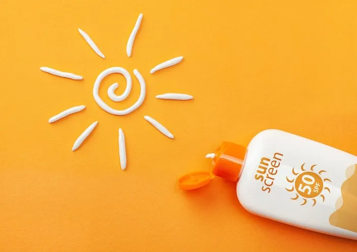 sunscreen on orange background plastic bottle of sun protection and white sun-shaped cream