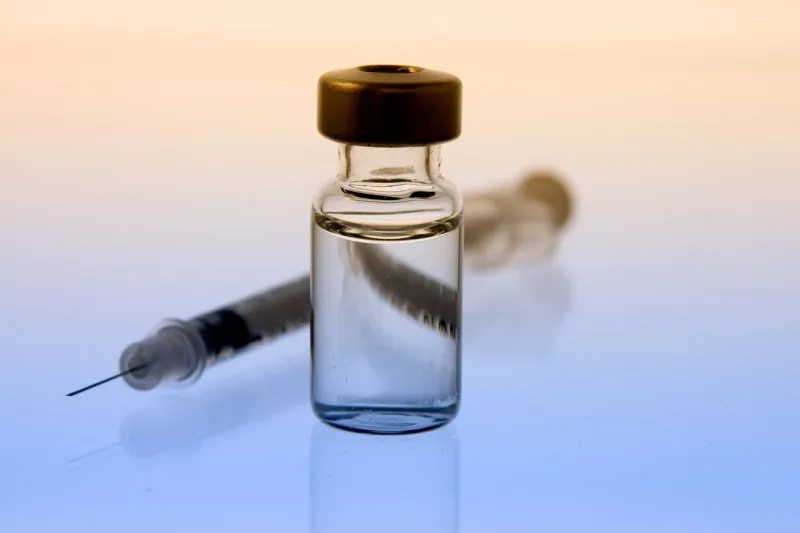 horizontal photo of clear liquid in a vial in front of a syringe